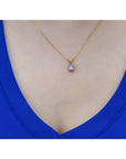 Gold necklace with a purple cabochon solitaire sapphire pendant on a person wearing a blue top.