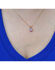 Gold necklace with a purple cabochon solitaire sapphire pendant on a person wearing a blue top.