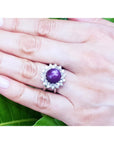 Red purple cabochon star ruby women's ring on a hand against a green leaf background