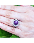 Red purple cabochon star ruby women's ring on a hand against a green leaf background