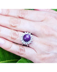 Red purple cabochon star ruby women's ring on a hand against a green leaf background