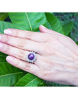 Hand wearing Red purple cabochon star ruby women's ring against a green leaf background