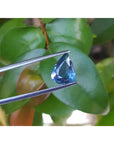 3.71 ct untreated pear-cut natural blue sapphire held by tweezers against green leaves.
