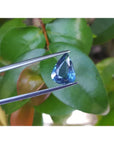 3.71 ct untreated pear-cut natural blue sapphire held by tweezers against green leaves.