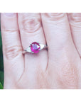 Oval cut ruby ring and trillion side diamonds on a finger against a blurred green background