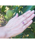 Hand wearing an oval cut ruby ring and trillion side diamonds against a green leafy background