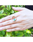 14K gold Circle of Life emerald pendant with natural diamonds, worn on a hand against green leaves.