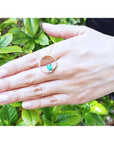 14K gold Circle of Life emerald pendant with natural diamonds, worn on a hand against green leaves.