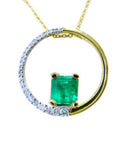 A yellow gold circle of life pendant necklace with a center square natural colombian emerald topside displayed.