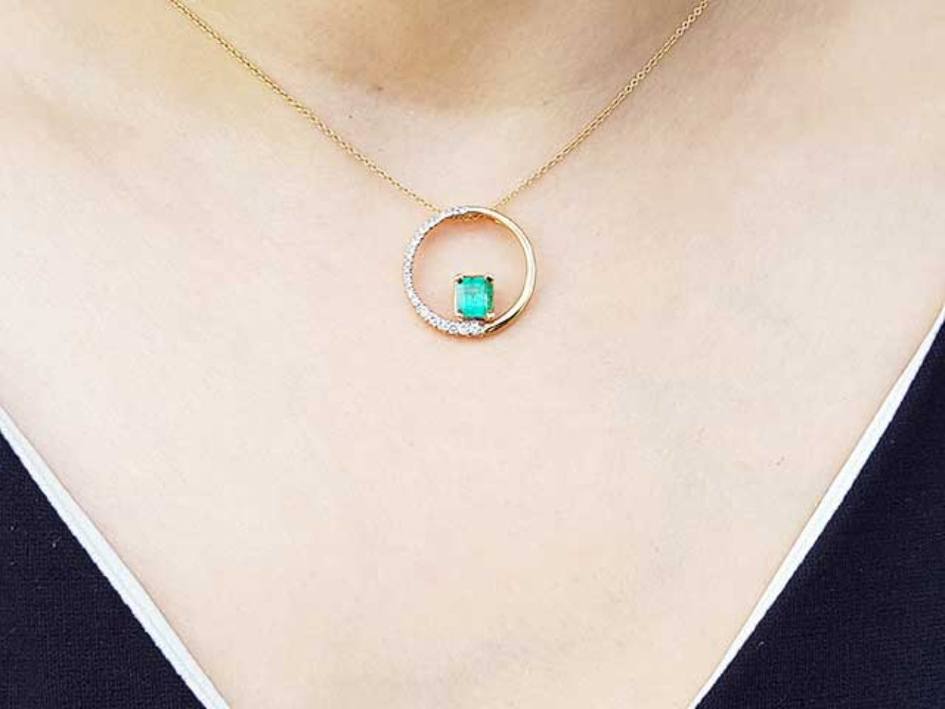 Gold necklace with an emerald circle of life pendant on a person's neck.