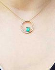 Gold necklace with an emerald circle of life pendant on a person's neck.