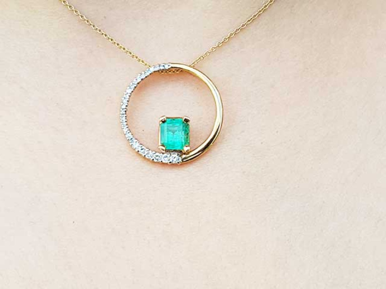 Gold necklace with a circle of life emerald pendant on a beige skin background.