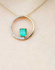Gold necklace with a circle of life emerald pendant on a beige skin background.