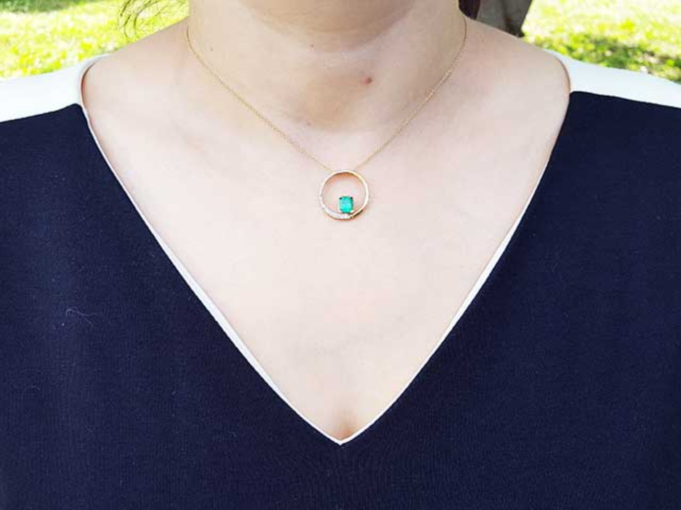 Necklace with a circle of life emerald pendant on a woman wearing a dark blue top.