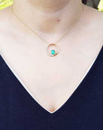 Necklace with a circle of life emerald pendant on a woman wearing a dark blue top.