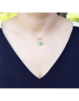14K gold "Circle of Life" emerald pendant with diamonds, worn on a woman's neck.