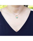 14K gold "Circle of Life" emerald pendant with diamonds, worn on a woman's neck.