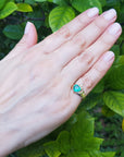 Hand wearing a heart emerald claddagh ring against a natural leafy background.