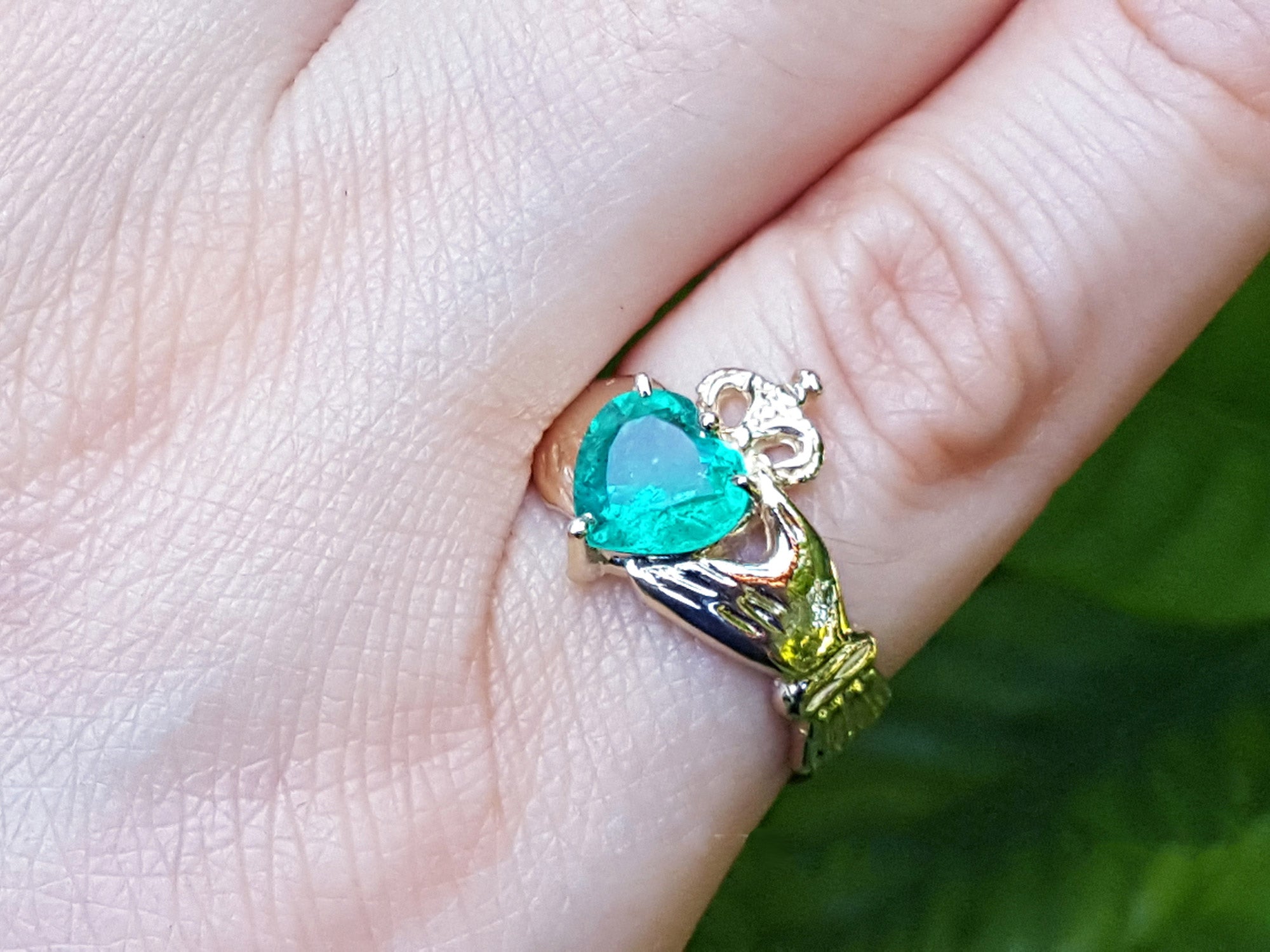 A close-up view of an emerald Claddagh ring on a finger