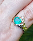 A close-up view of an emerald Claddagh ring on a finger