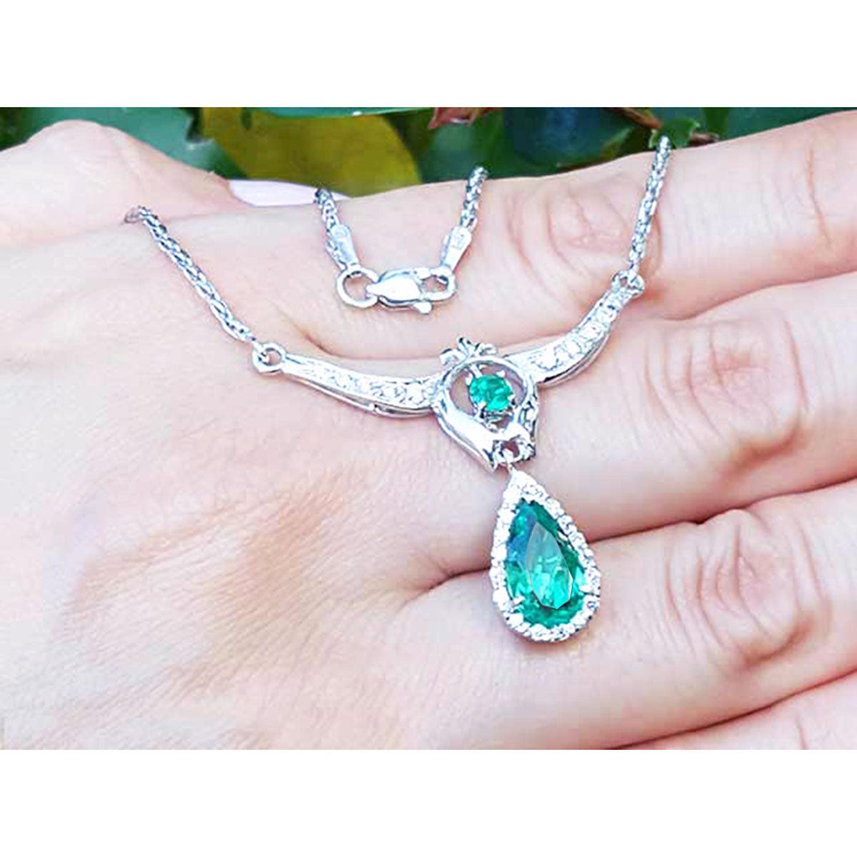 A close view of a hand displaying a genuine emerald necklace with chain May birthstone pear-shaped 14k white gold