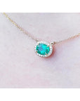 Oval Muzo emerald necklace with diamond halo on a delicate 14K yellow gold chain.