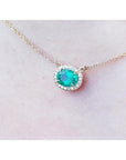 Oval Muzo emerald necklace with diamond halo on a delicate 14K yellow gold chain.