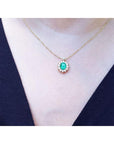A close sight of a gold necklace with a oval Muzo emerald gemstone pendant on a person wearing a dark blue top.