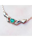14K yellow gold Claddagh necklace with a heart-cut emerald held by two hands, worn on a neck.