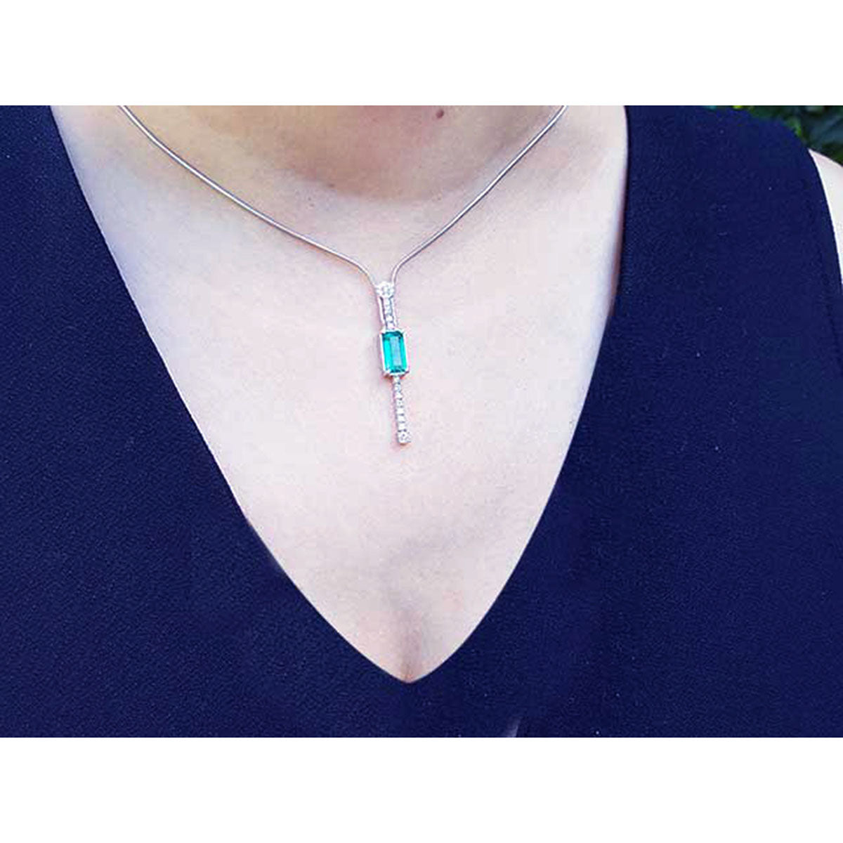 White gold necklace with a natural Colombian emerald pendant on a woman wearing a dark blue top.