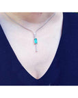 White gold necklace with a natural Colombian emerald pendant on a woman wearing a dark blue top.