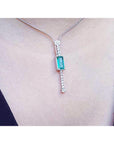 Close view of a white gold necklace with an emerald gemstone pendant on a person's neck