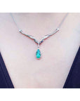 A close view of a necklace with a emerald stone teardrop pendant on a person wearing a dark top.