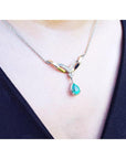 A close view of a necklace with a dangling teardrop-shaped emerald pendant on a woman wearing a black top.