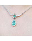 On a close view a white gold necklace with a teardrop-shaped emerald pendant on a plain background