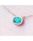 0.90 carat oval Muzo emerald necklace with diamond halo on a 14K yellow gold chain.