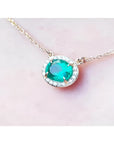 0.90 carat oval Muzo emerald necklace with diamond halo on a 14K yellow gold chain.