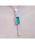 White gold women's necklace with a rectangular Colombian emerald and diamond accents, worn on a neck.