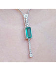 White gold women's necklace with a rectangular Colombian emerald and diamond accents, worn on a neck.