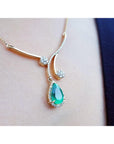 close side view of a yellow gold necklace with an emerald teardrop pendant on a woman's collar