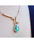 close side view of a yellow gold necklace with an emerald teardrop pendant on a woman's collar