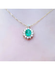 Oval cut 1.11 ct. emerald and natural diamond cluster necklace on a 14K yellow gold chain.