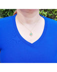 14K gold clover pendant with a square emerald and diamonds, worn on a woman in a blue shirt.
