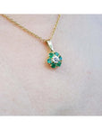 A yellow gold emerald and diamond cluster pendant necklace on a light skin background.