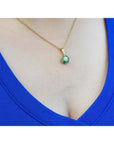 18K yellow gold cluster pendant with deep green emeralds and a center diamond on a woman's neck.