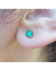 Medium deep green emerald stud earring in 14K yellow gold with three prongs, worn on an ear.
