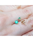 Round medium deep emerald stud earrings in 14K yellow gold with three prongs, held on a hand.