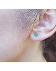 Cocktail emerald stud earring with a medium deep green gemstone in 14K yellow gold, worn on an ear.
