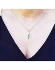 White gold 14k emerald briolette necklace with a pendant worn by a person in a dark blue top.