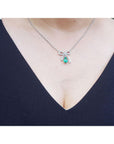 18k white gold bowtie necklace with a Colombian emerald pendant worn by a lady in a navy blue top.
